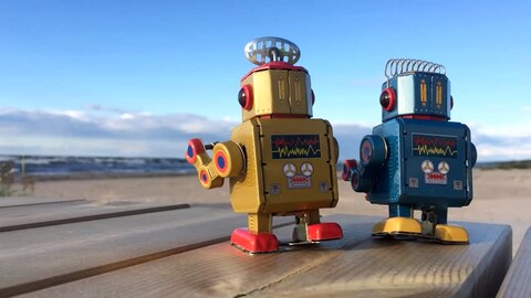 two old school box style robots on a table near the beach looking at the water in the distance